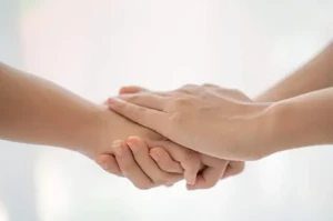 De rechterhand van een client licht ontspannen in de handen van de haptonoom.