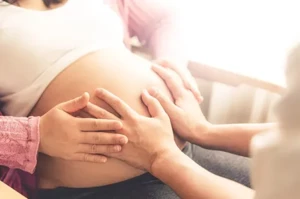Een hoogzwangere blote buik liefdevol aangeraakt door de handen van de zwangere en de haptonoom.